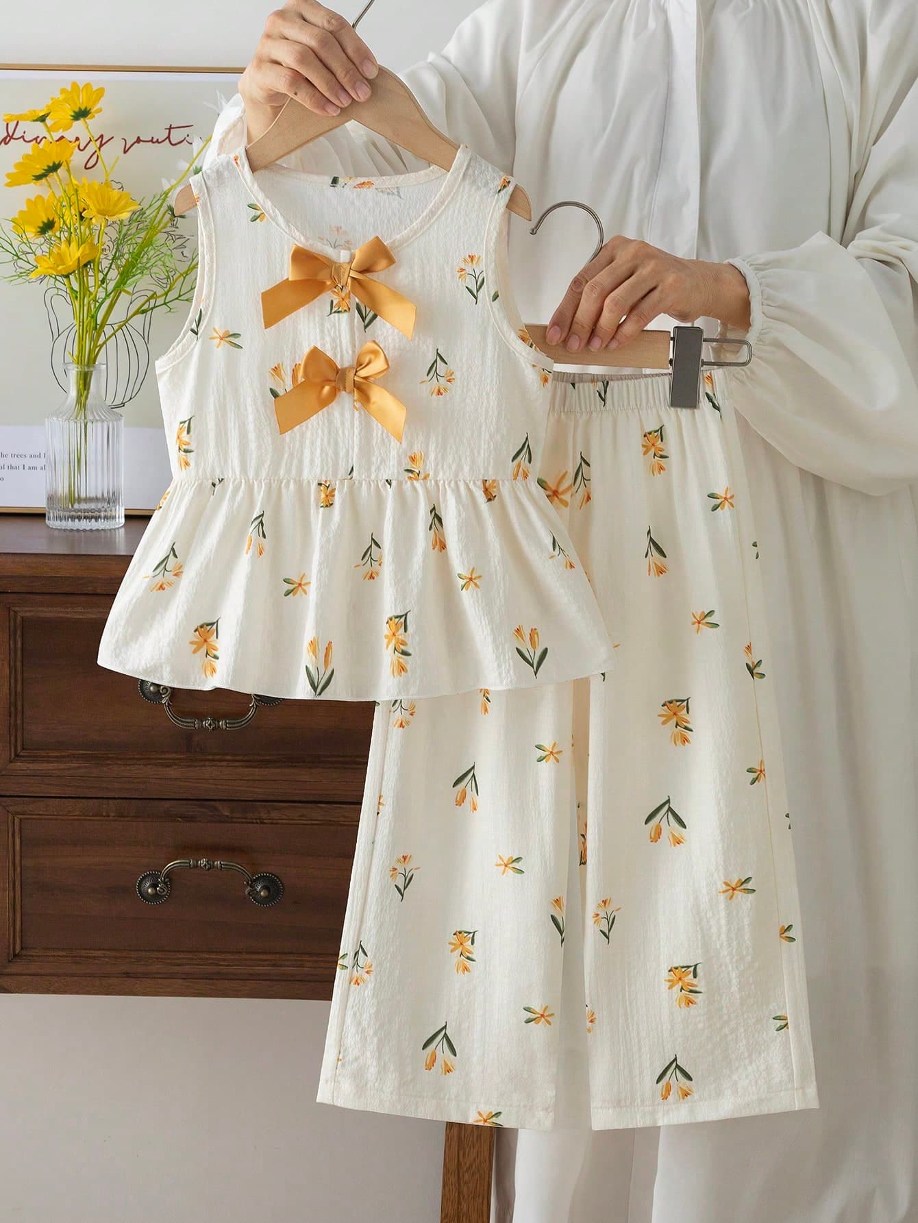 This Set Of Girls' Clothes Uses A Light Yellow Tone, With An Overall Fresh And Cute Design. The Top Has A Sleeveless Design, And The Neckline Has A Yellow Bow Decoration. The Clothes Have Delicate Small Patterns, With A Lightweight And Comfortable Material, Suitable For Spring And Summer Wear, And Outdoor Activities.