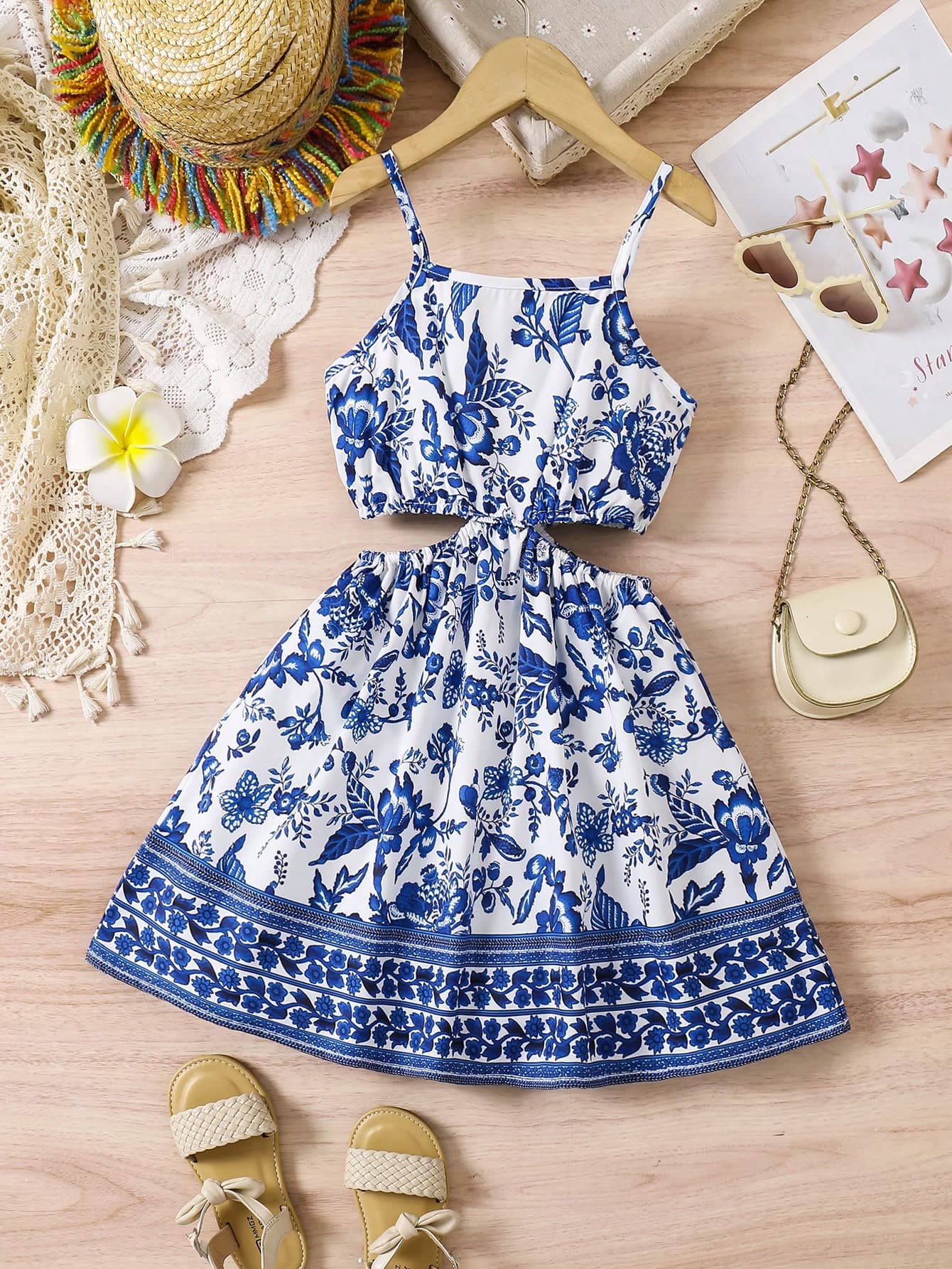 Young Girl Vacation-Style Camisole Dress Featuring A Youthful Blue Floral Placement Print And A Cut-Out Design At The Waist.