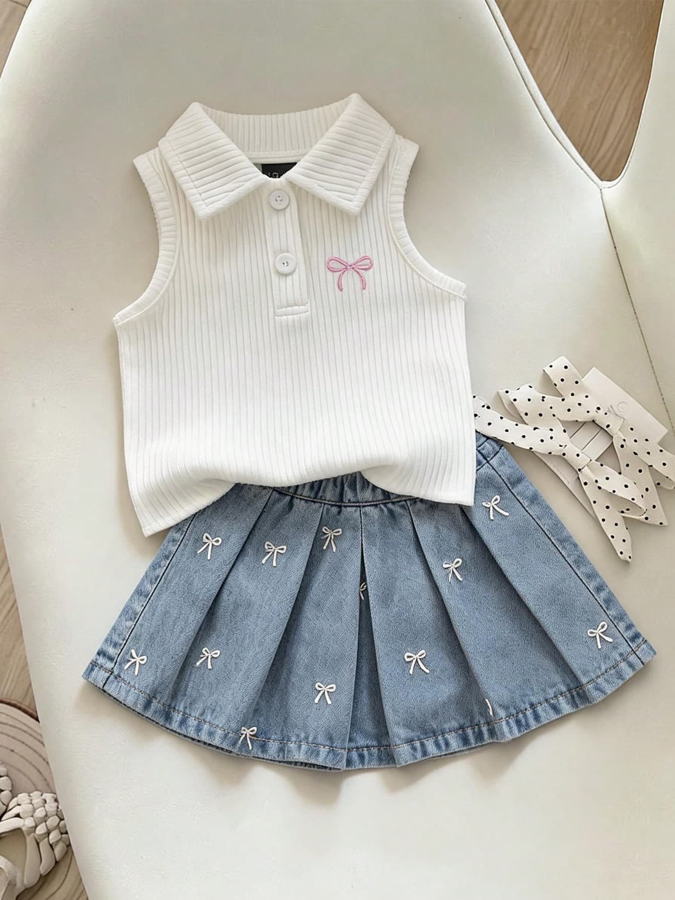 Vintaside Kids Baby Girls' Short Sleeve Sleeveless Set, Ivory Top + Light Blue Denim Skirt. The Top Is A Sleeveless, Stretchy Polo Collar Knit Design With A Pink Bow Embroidery On The Chest. The Skirt Is A Light Wash Denim Short Skirt With White Embroidered Bow Details. The Overall Style Is Sweet, Cute And Collegiate, Suitable For Summer Wear, Daily Outings, Preschool, Parties And Family Leisure Occasions.