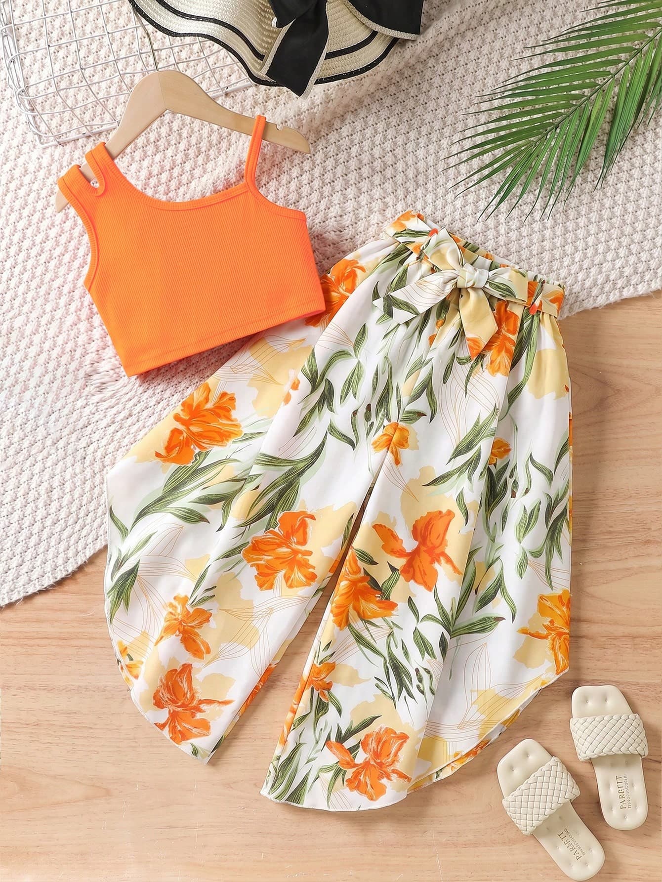 SHEIN Young Girls Summer Vacation Style 2-Piece Set, Designed For Spring/Summer Outings. The Top Is A Bright Orange Ribbed Cropped Camisole With A Slim Fit Elastic Design That Hugs The Body, Vibrant And Eye-Catching, Exuding A Youthful Energy. The Bottom Is A Pair Of Draping Wide-Leg Long Pants With A White Base And Large Orange Floral Prints, Creating A Tropical Vibe. The Bow Tie Waistband Not Only Accentuates The Waistline But Also Adds Layers To The Outfit. The Loose Fit Of The Pants Is Inclusive Of Various Leg Types, Suitable For Daily School, Beach Vacations, And Park Outings, Making It An Eye-Catching Essential For The Spring/Summer Wardrobe.